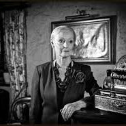 Black and white portrait of a woman sitting at a desk with a vintage map in the background.