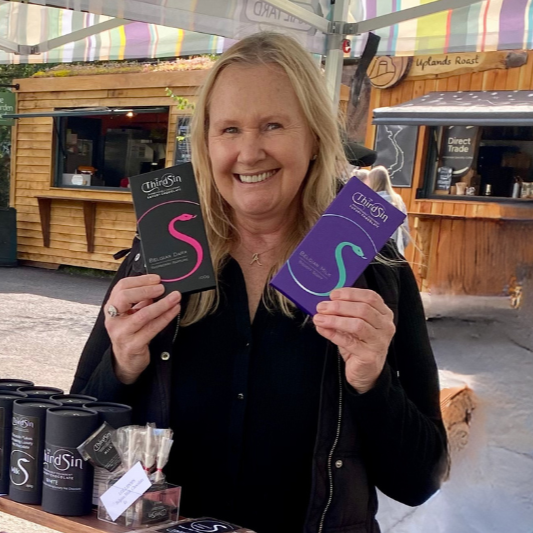 Woman holding purple boxes at a table with more boxes and products.