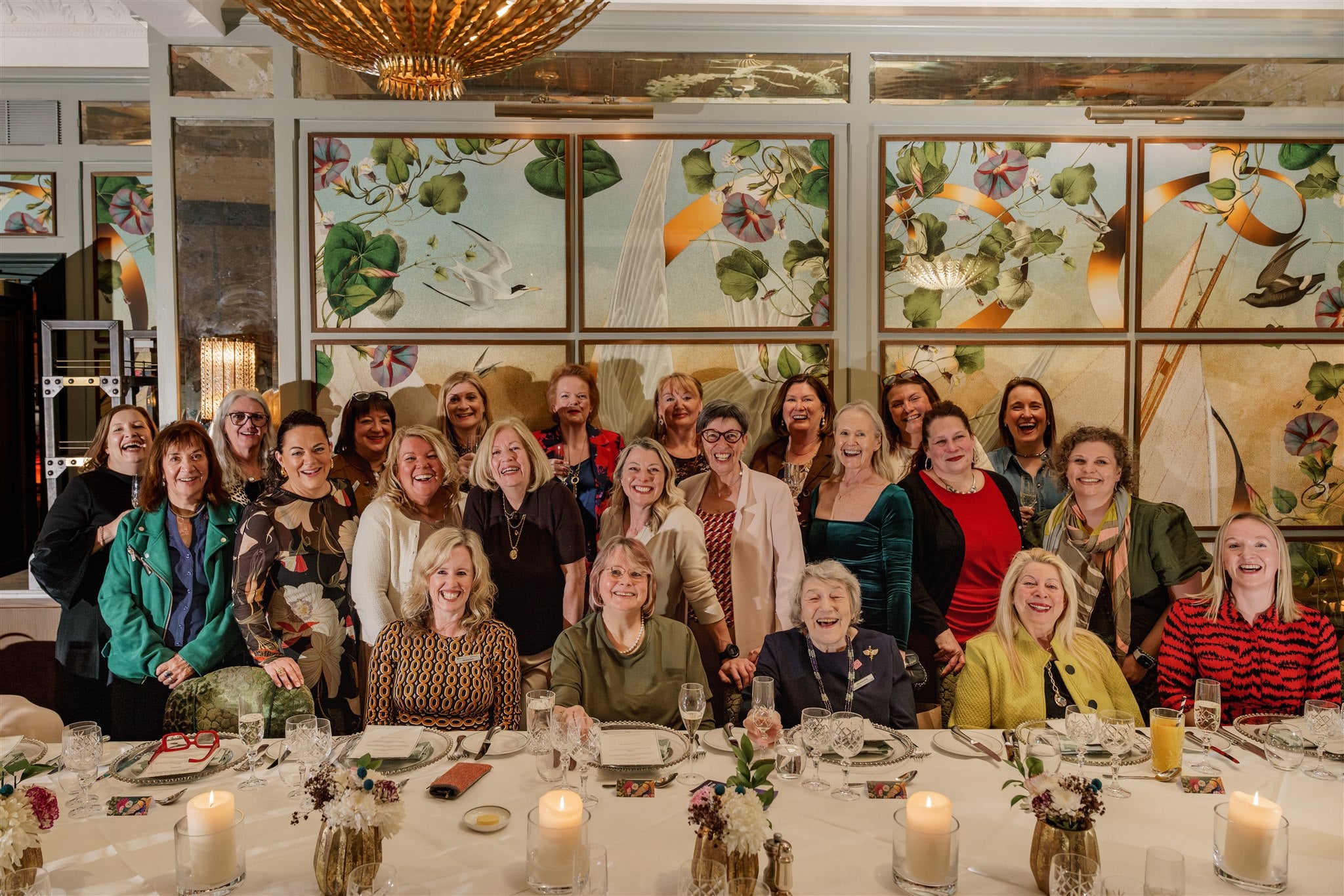 Group of people posing together at a formal event with floral wall art in the background.