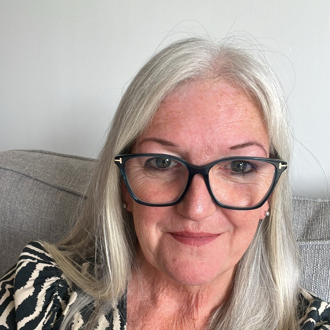Woman with glasses and a patterned top sitting on a couch.